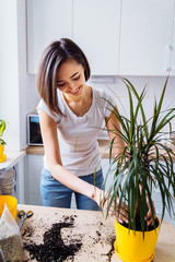 Beautiful smiling girl with braces replanting a indoor flower. Wearing a white T-shirt and blue...