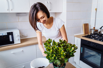 Beautiful smiling girl with braces replanting a indoor flower. Wearing a white T-shirt and blue...