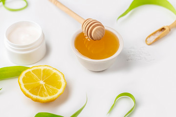 Natural organic ingredients to make home skin care. Cleansing and nourishing cosmetics. Beauty products: cream, honey, sea salt among green leaves on white background. Close up, copy space for text