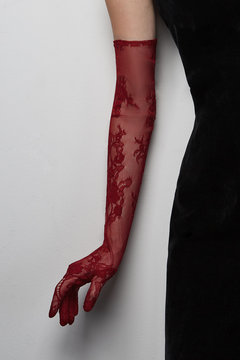 Cropped shot of a lady in a black tight dress and a burgundy evening glove against the gray wall. The elegant elbow glove is made of the lace fabric with floral pattern. 