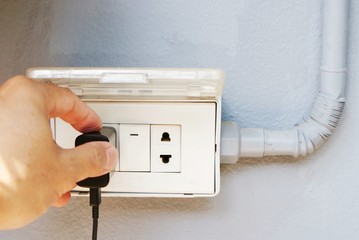 Close up left hand of a man is holding plug and put into the socket for charging mobile phone, Abstract soft focus background.
