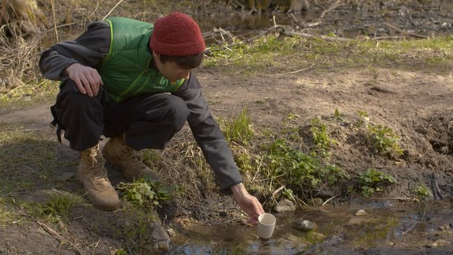 Young handsome man drinking water from a forest river. Concept of natural purity. Bright and sunny early sping day.