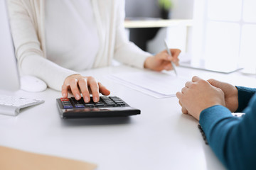 Accountant checking financial statement or counting by calculator income for tax form, hands closeup. Business woman sitting and working with colleague at the desk in office toned in blue. Tax and
