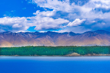 Lake landscape with a green forest  and mountains under cloudy sky