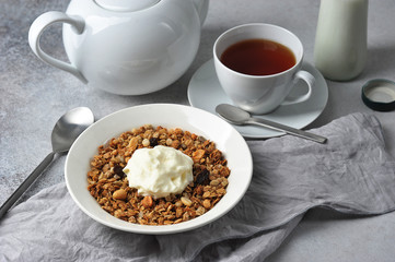 Muesli with nuts, seeds and raisins.  A cup of tea and a bottle of milk complete the composition.  Light background.  Close-up.