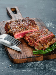 Beef steak with coarse salt and a sprig of rosemary on a wooden cutting board against a dark background