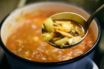 Ladle with minced meat soup. Blurred cooking pot on background.