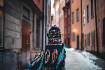 Fototapeta premium A colorful woman in colorful clothes and a hood on a sidewalk