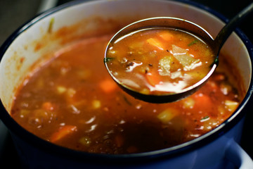 Cabbage soup. Blurred cooking pot on background. Focus in ladle.