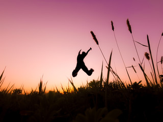 Silhouette of girl jumping in field at sunset with dramatic pink sky in the background