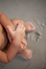 A small child plays in the sand on the beach. Only arms and legs are visible.