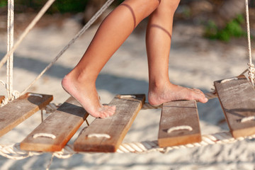 Little feet of a child walk on a rope bridge on the beach in the sunset.