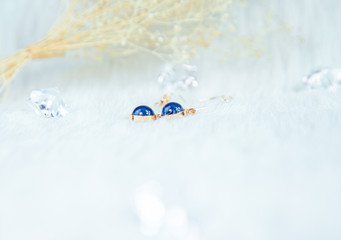 Close-up of blue metal earrings.Made of blue round beads and golden yellow metal.  Down blankets and beautiful dried flowers are used as decorations.  Transparent ice cube props.