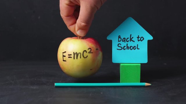 A man rotates an apple with the written formula e = mc2 next to the sticker back to school