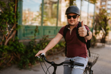 Young caucasian cyclist with helmet and sunglasses on a bicycle in front of the window