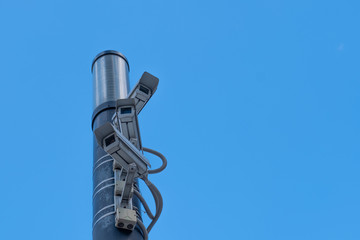 Three surveillance cameras on a pillar against the sky