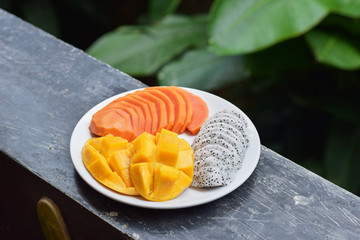 Plate with tropical fruits. Papaya, mango, dragon fruit on a plate on a green background. Thai fruits.