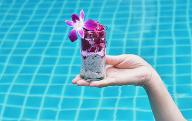 glass with tropical dessert on hand on a background of blue pool