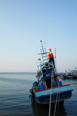 A fishing boat held by ropes facing towards vastness of sky and sea. Shot from behind.