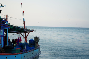 Obraz premium A fishing boat facing towards vastness of sky and sea. Birds are flying on the sky. Shot from right side.