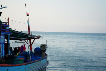 A fishing boat facing towards vastness of sky and sea. Birds are flying on the sky. Shot from right side.