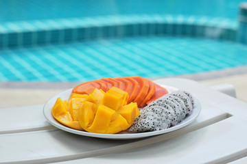 Plate with tropical fruits near the pool. Papaya, mango, dragon fruit on a plate on a blue pool background. Thai fruits.