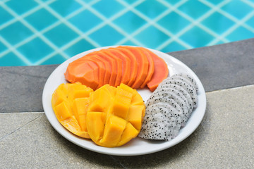 Plate with tropical fruits near the pool. Papaya, mango, dragon fruit on a plate on a blue pool background. Thai fruits.