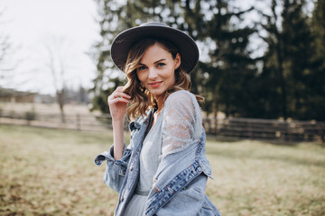 Portrait of the bride. Country style. A young girl in a blue gray wedding dress, denim jacket and hat with a bouquet of flowers and greenery in her hands on a background of a forest and a wooden fence