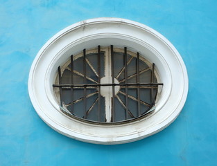 An oval barred window in a blue wall