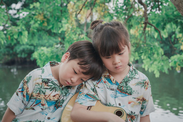 Lovely twin boy and girl stay at home to safe from virus. Lovely twin boy and girl sit leisurely and playing guitar at riverside home. Stay home stay safe concept protect you from virus.