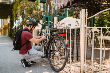 A young caucasian cyclist locks a bicycle by the fence