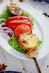 Grilled vegetables - potato, tomato, bell pepper, eggplant and zuccini on skewer over a white plate.