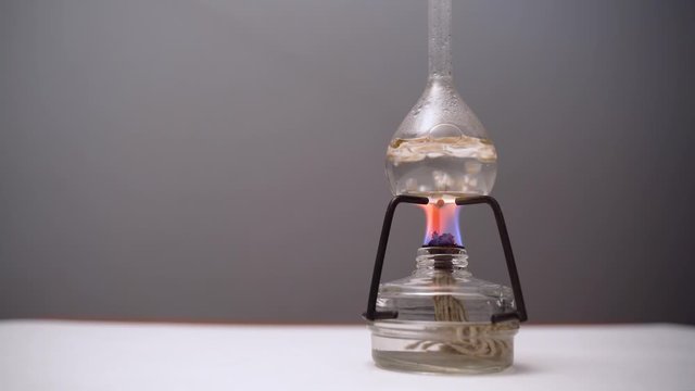 Bulb with boiling liquid on the burner flame. Flask is heated on the burner in laboratory. Scientific experiment. Glass alcohol burner burns on a table. Preparation Covid-19 vaccine.