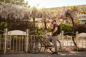 Obraz premium A handsome caucasian cyclist with a backpack, glasses and helmet talks on the phone