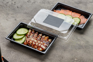 Fresh sliced salmon and smoked eel fillet with cucumber in plastic boxes ready for delivery. Wild atlantic fish. Copy space
