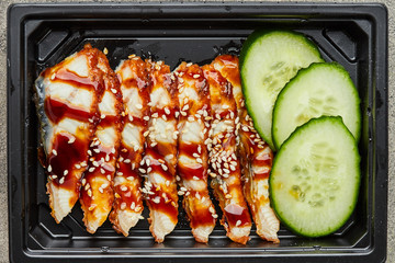 Sliced smoked eel fillet with cucumber in plastic box ready for delivery
