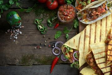 burritos, quesadillas and tacos on a wooden background with vegetables