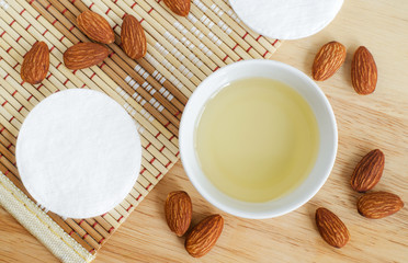 Small white bowl with almond oil and cotton pads for natural skin care. Organic cleansing oil, make up remover. Top view, copy space.