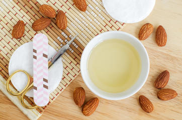 Small white bowl with almond oil, scissors and nail file for natural nails and cuticle treatment. Homemade manicure and pedicure concept. Top view, opy space.