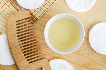 Olive oil, cotton pads and wooden hairbrush. Ingredients for preparing homemade hair mask. Natural beauty treatment recipe and zero waste concept. Top view, copy space.