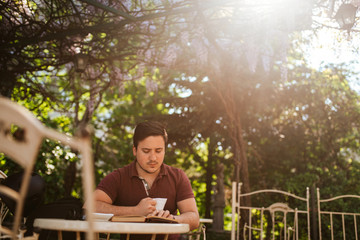A young caucasian man in a cafe garden is reading a book