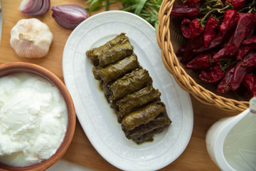 Delicious dolma sarma rice, white yogurt sauce . Garlic, red onion, tarragon . In a stuffed white plate . Yogurt and dried beans in a brown bowl . Red Dry Pepper in Traditional Basket .
