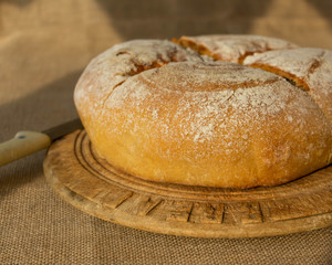 A baked freshly baked loaf of bread sitting on top of a cutting board on a hessian back drop with space for text