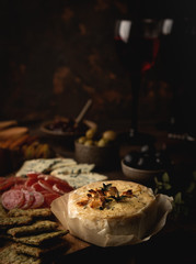 baked camembert cheese with jam, sausage, blue cheese, olives and snacks, on a wooden board, glasses with red wine