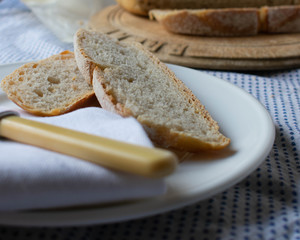 A close up of slices of sourdough served on a white side plate with a bone handle butter knife on top of a farmhouse kitchen table cloth.