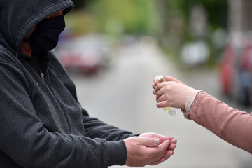 Close-up of an older man in a dark hoodie and young woman's hands apllying hand sanitizer gel on the hands of an older man.