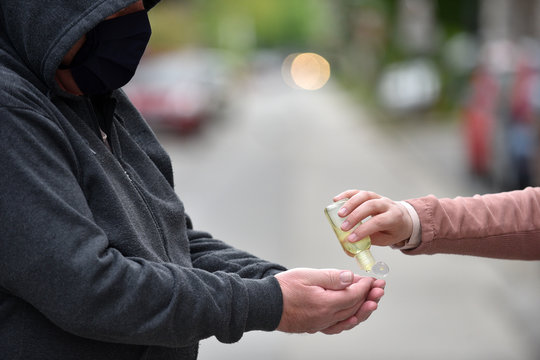 Close-up of an older man in a dark hoodie and young woman's hands apllying hand sanitizer gel on the hands of an older man. - Powered by Adobe