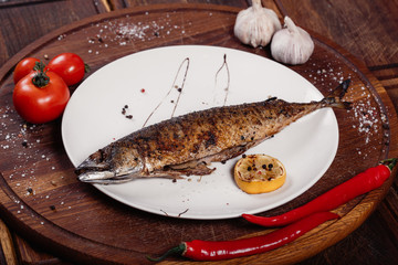 Appetizing mackerel fish baked on fire with spices, served on a plate and decorated with vegetables