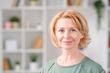 Smiling mature woman with under eye patches having beauty procedure at home