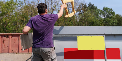 Plump,dark-haired,middle-aged man throws wooden planks and furniture parts into containers at station of collection of large-size garbage in Germany,Europe.Sunny day.Back view.Selective focus.Mockup